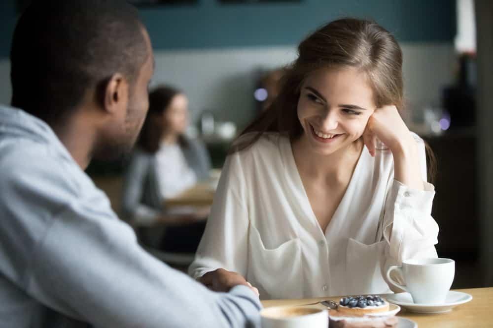 Happy interracial couple flirting talking sitting at cafe table