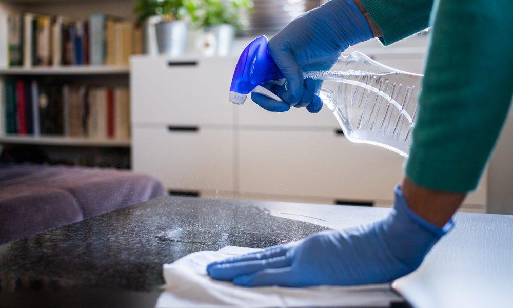 A close-up of someone wearing latex gloves and using bleach to safely disinfect their home. Are you wonder if bleach is safe to clean with? Here