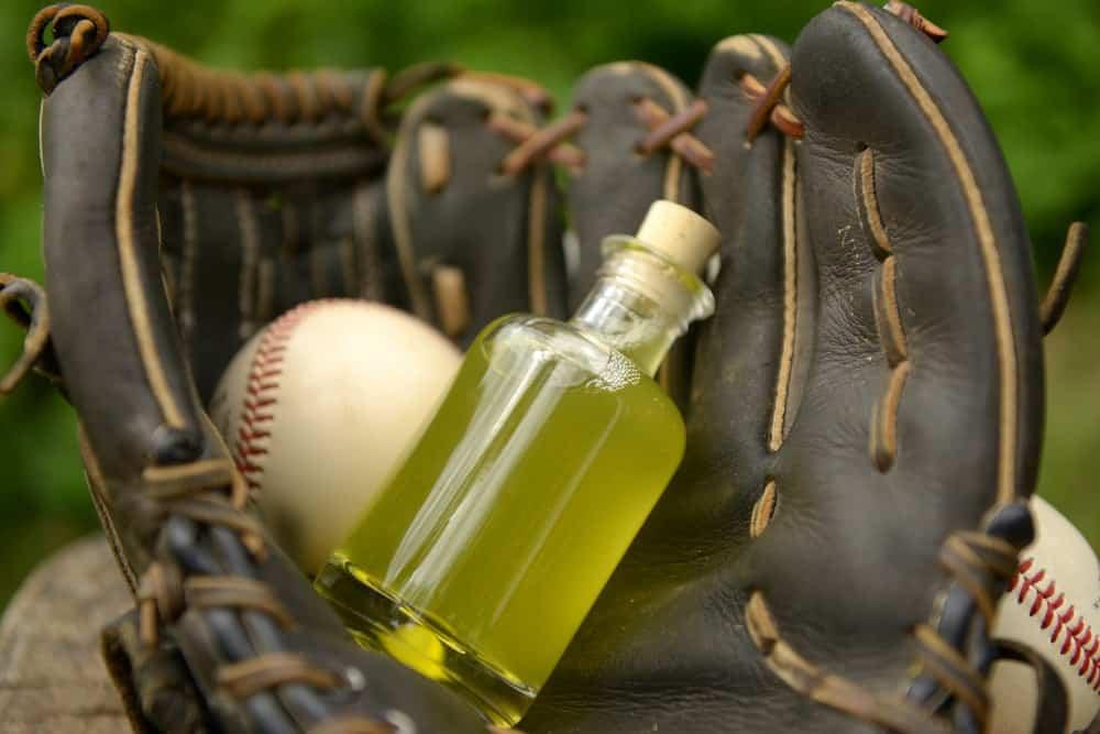 A close look at a leather baseball glove, ball and a bottle of oil.