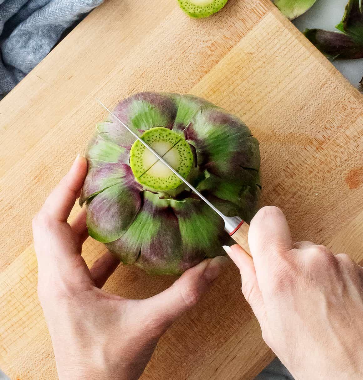 Hands scoring artichoke stem with knife