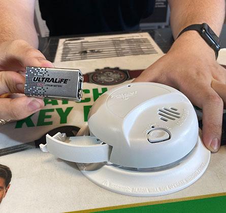 Hands taking lithium battery out of smoke detector