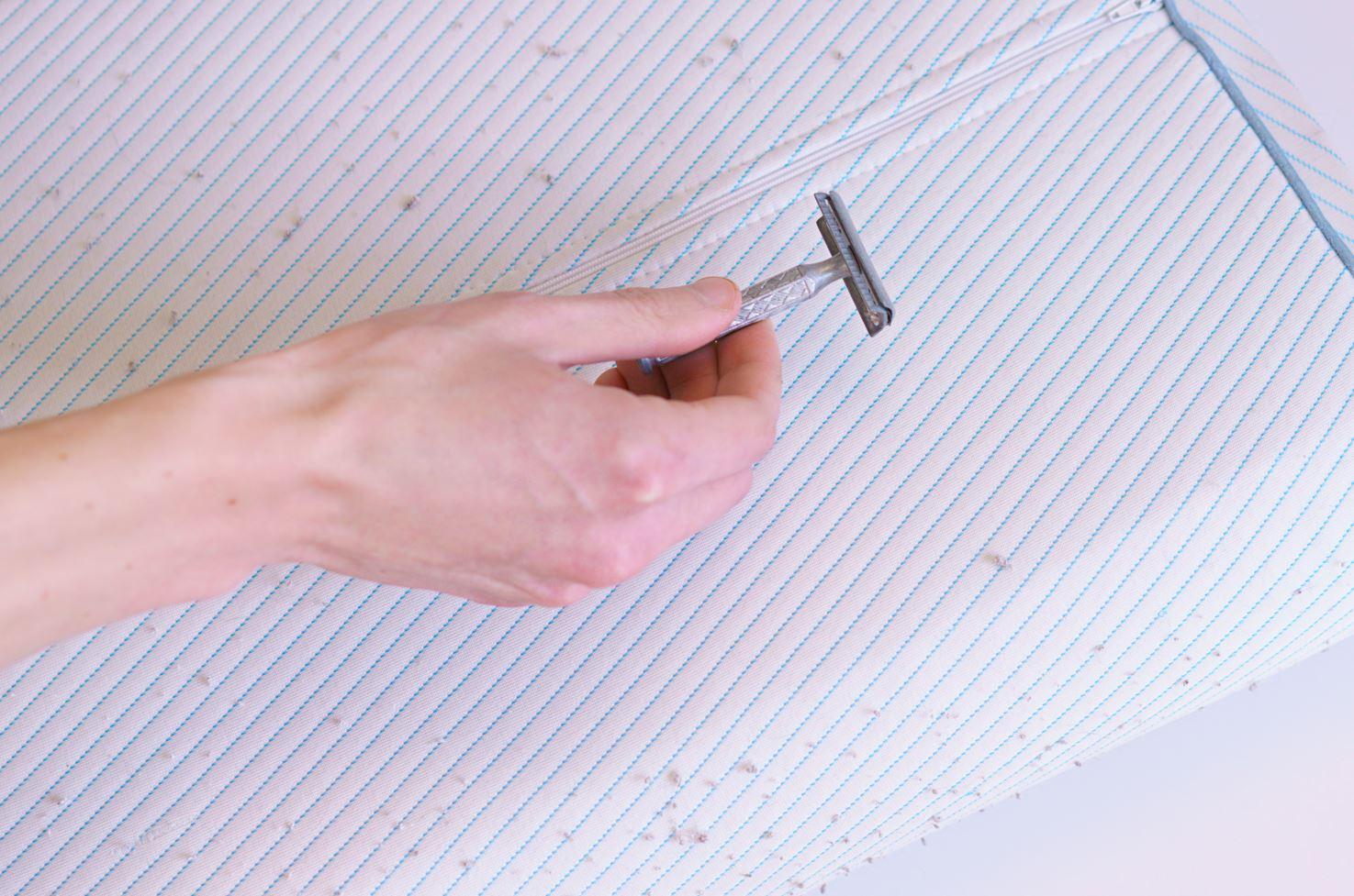 man using razor to remove lint from white mattress