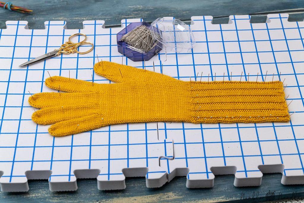 the finished glove on a blocking board to improve the stitch definition with pins stretching the fabric in either direction