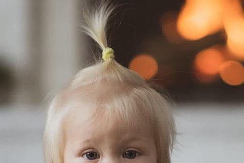 A blonde-haired baby with a single ponytail on top of her head