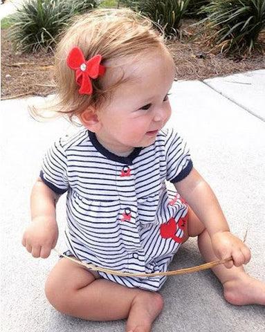 A baby with a red bow tie holding her fringe out of her face