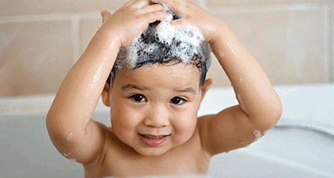 A baby in the bath holding their head full of shampoo