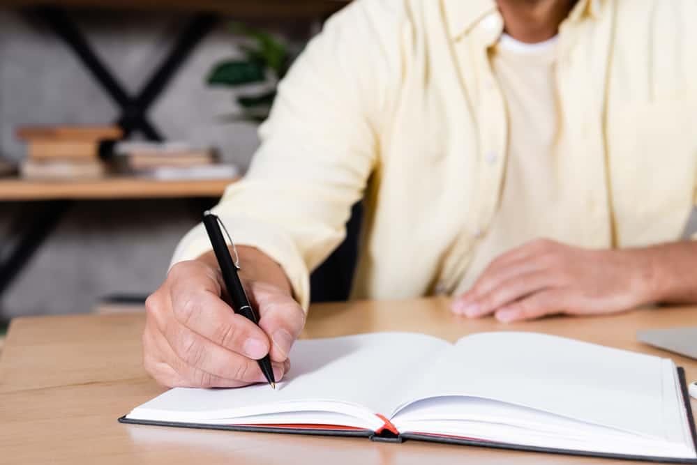 Partial view of man writing in notebook while working at home