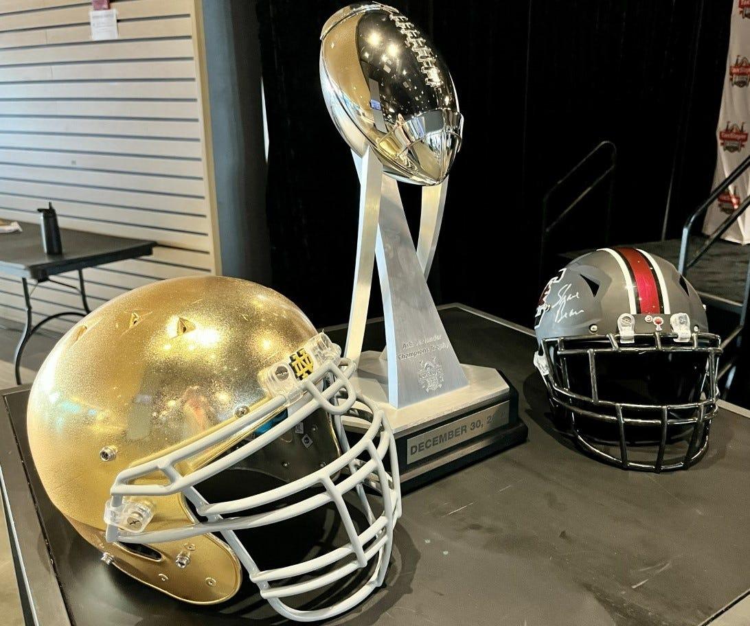 The helmets of Notre Dame (left) and South Carolina (right) flank the Ash Verlander Trophy for the winner of Friday