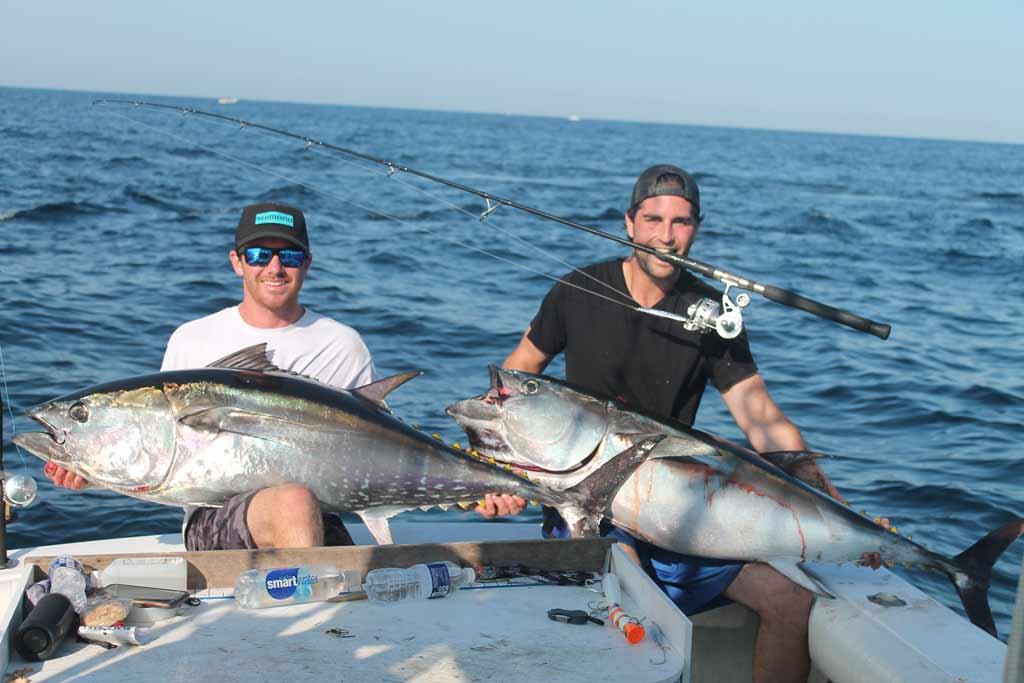 Two fishermen sitting on a boat, each holding a Tuna fish