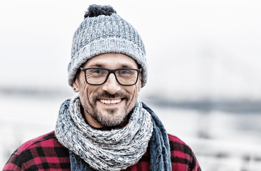 A portrait of a man in a knitted white-blue scarf and hat on cold weather is wearing glasses to protect his eyes from cold wind