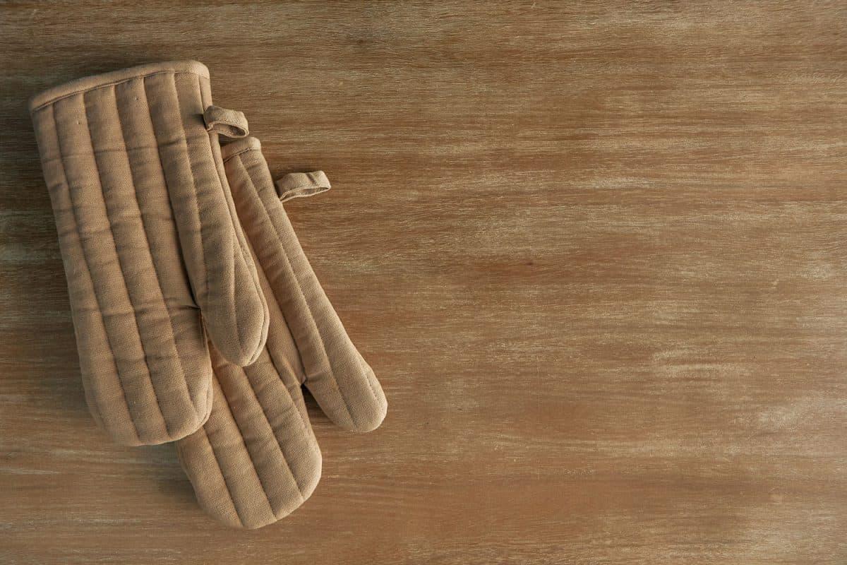 A pair of brown oven mitts on top of a wooden table