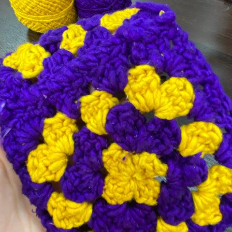 A close up image of one of the purple and yellow worsted weight granny squares.
