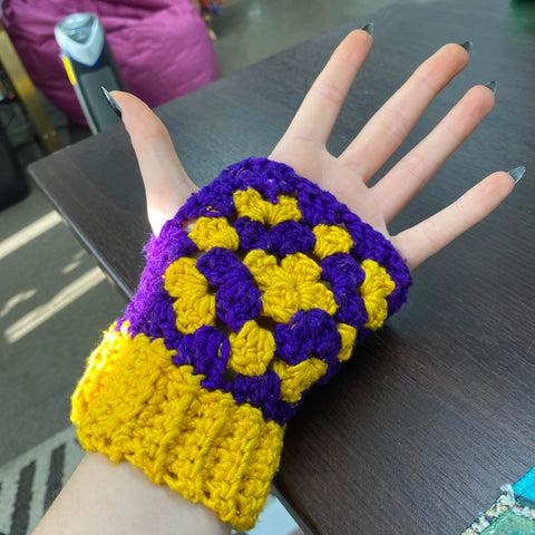 A hand, facing palm up, is sporting the finished purple and yellow granny square fingerless gloves.