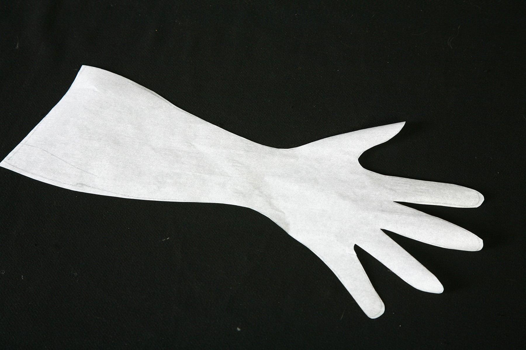 A spandex glove pattern that has been cut out of translucent paper, on a black background.