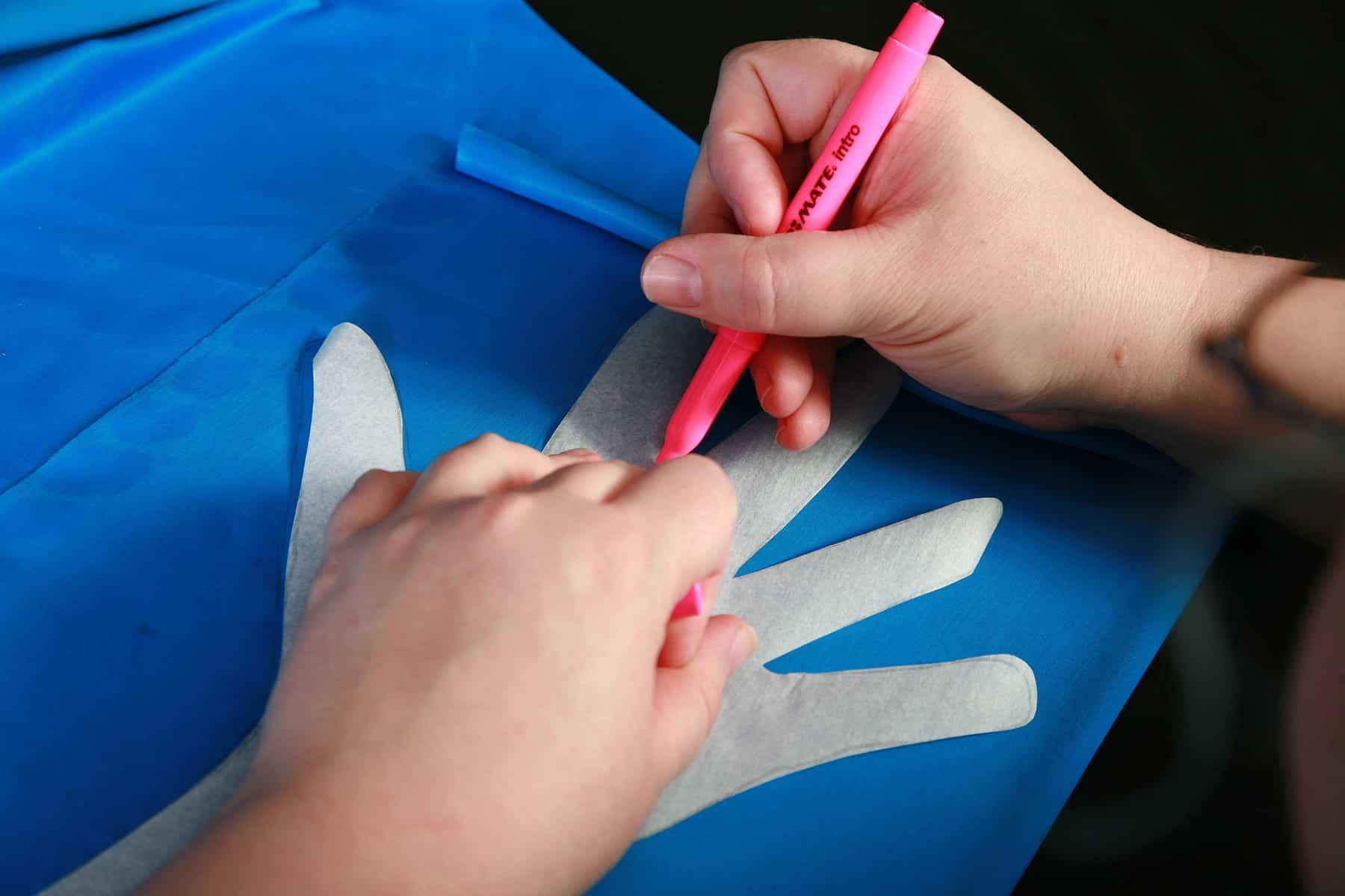 A glove pattern is being traced onto blue spandex fabric.