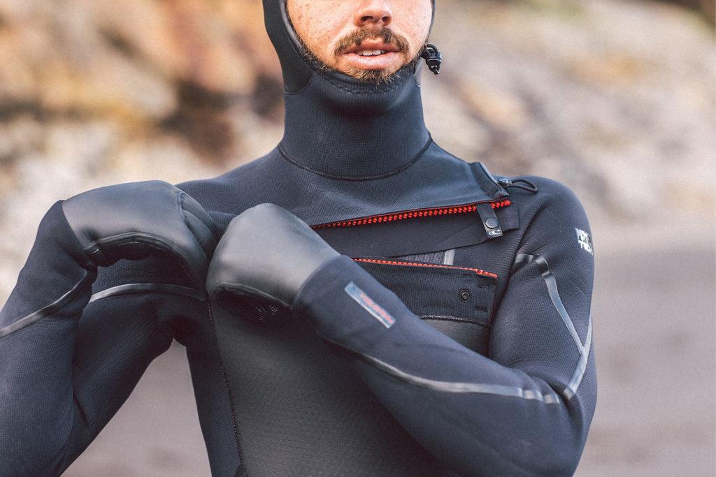 Man zipping up his chest zip wetsuit and wearing neoprene gloves
