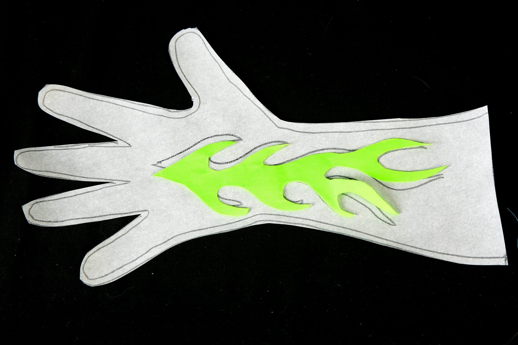 A glove pattern has been cut out of exam table paper. A neon green flame has been cut from fabric and placed on top.