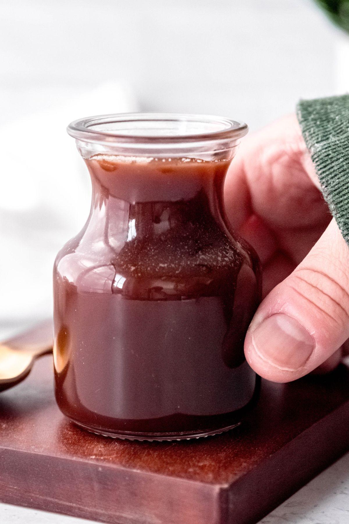 hand grabbing a jar of Irish cream syrup from a dark wooden cutting board.