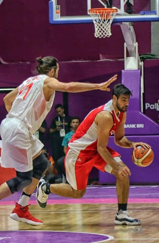 Basketball player in red tries to dribble around the player in white.