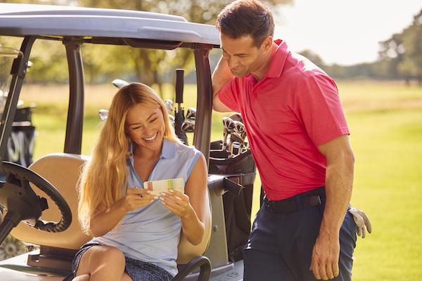 Couple Sitting In Buggy Playing Round On Golf And Checking Score Card Together
