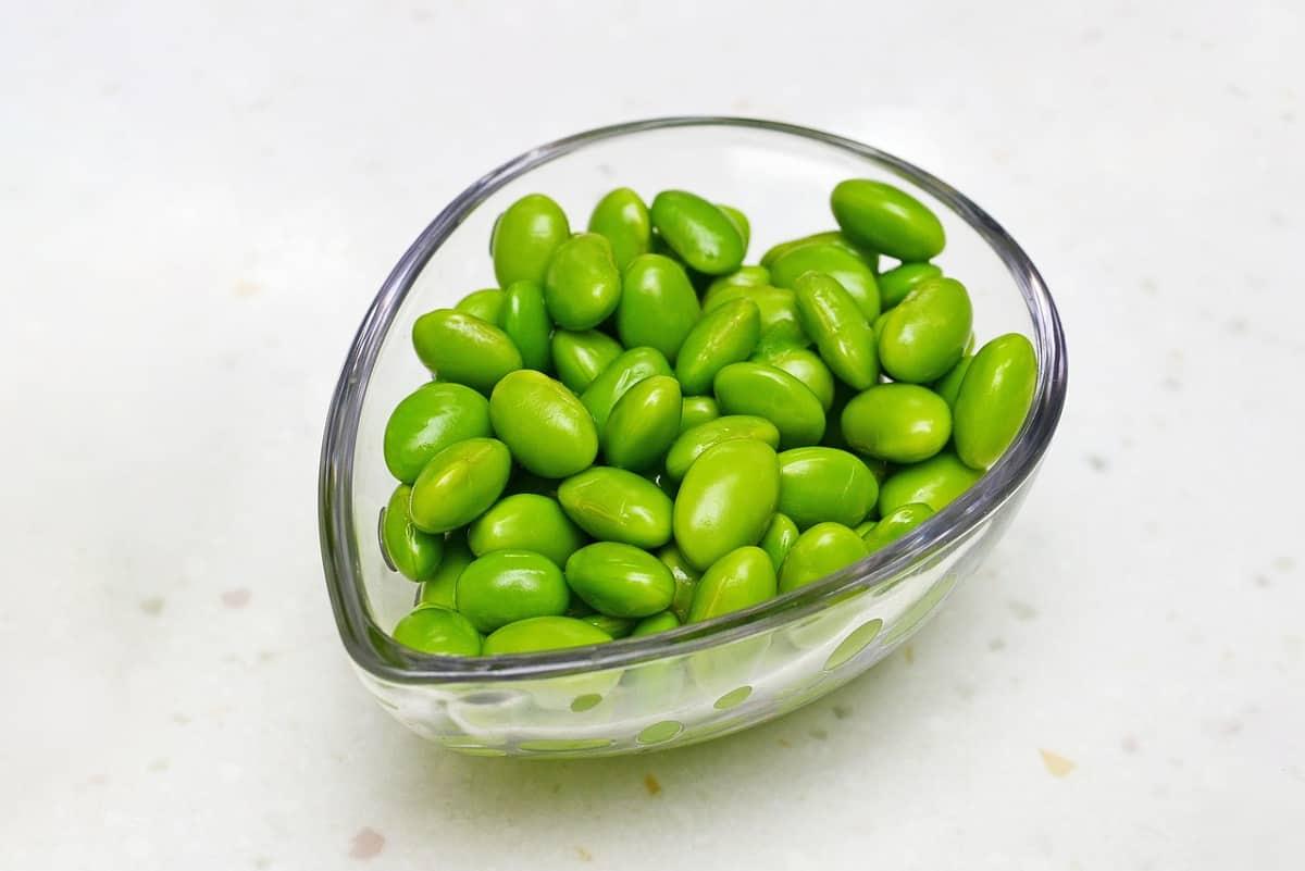 A glass bowl with shelled edamame (mukimame) on a white table