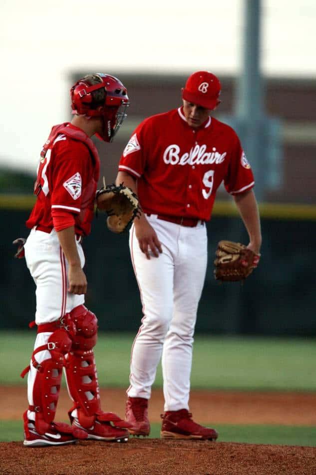 Pitcher and catcher in red jerseys meet at the mound.