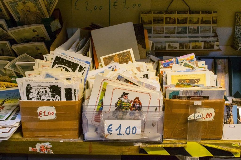 Pile of postcards for sale at Libreria Acqua Alta Venice. Bins are marked with 1 Euro price tag, travel souvenir ideas