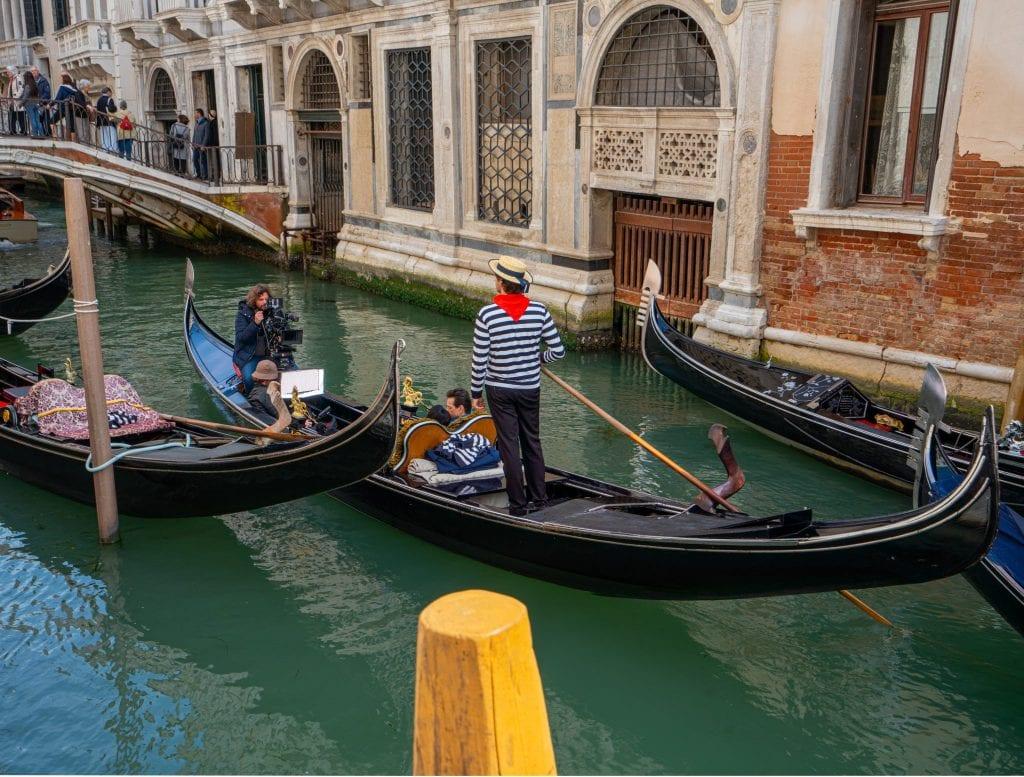 Gondola ride in Venice with a gondlier standing up in the center of the frame. The gondolier has a red bandana on.