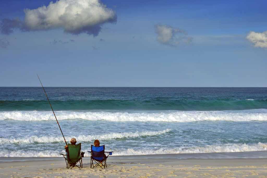 A couple sitting on a beach, fishing