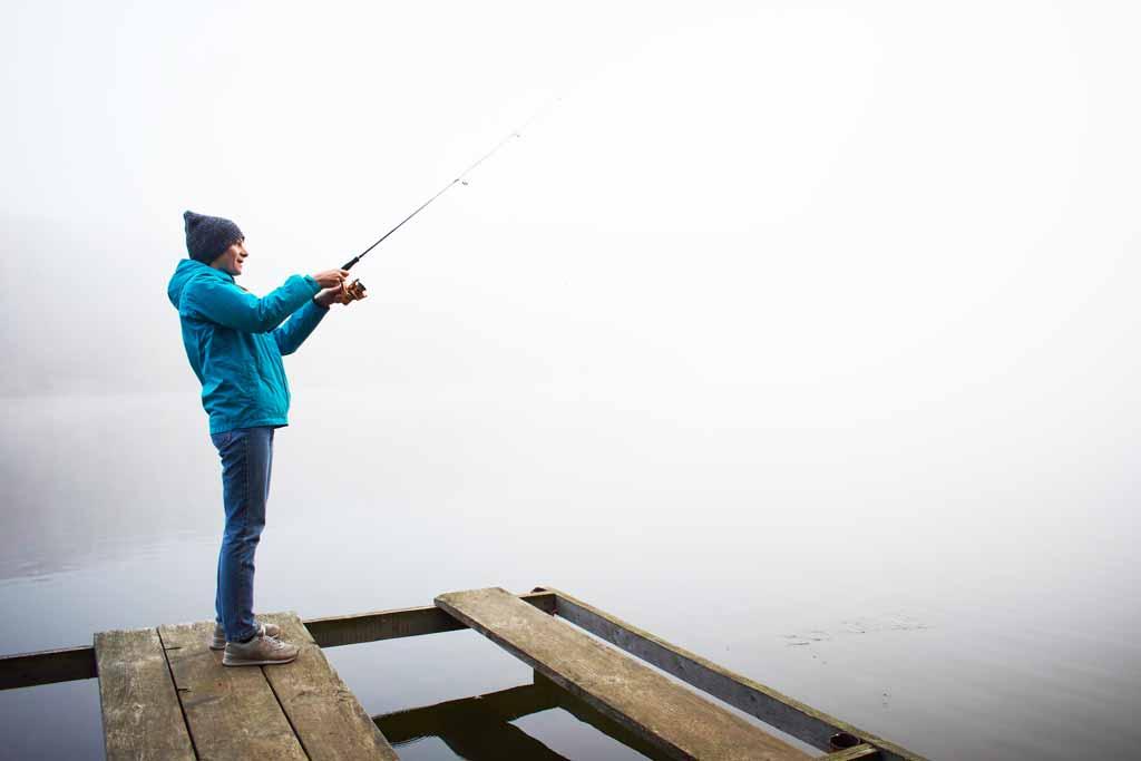 A woman angler in winter fishing gear fishing from a dock on a foggy day