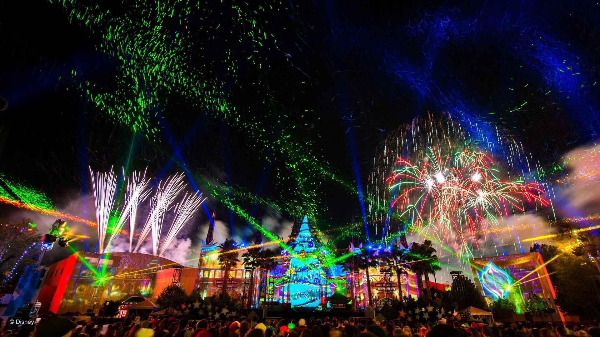 A crowd of people near buildings lit up with lights and lasers