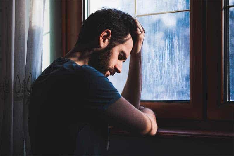 depressed man holding his head beside window