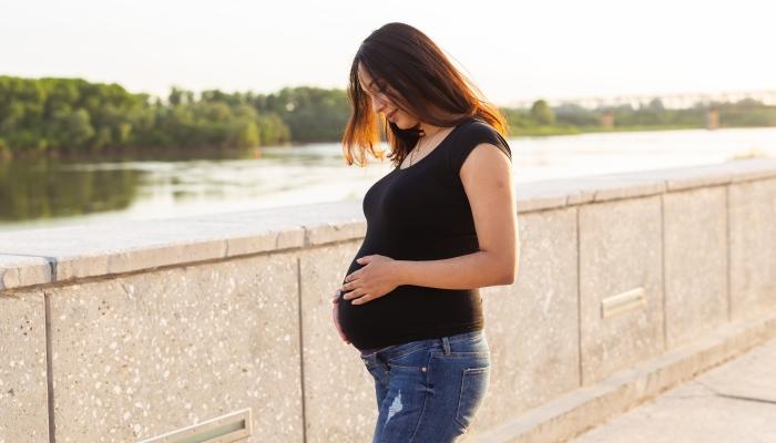Portrait of a hispanic pregnant woman walking on a curb at sunset.
