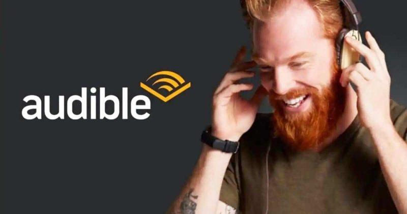 Audible logo. Man smiles holding headphones over his ears.