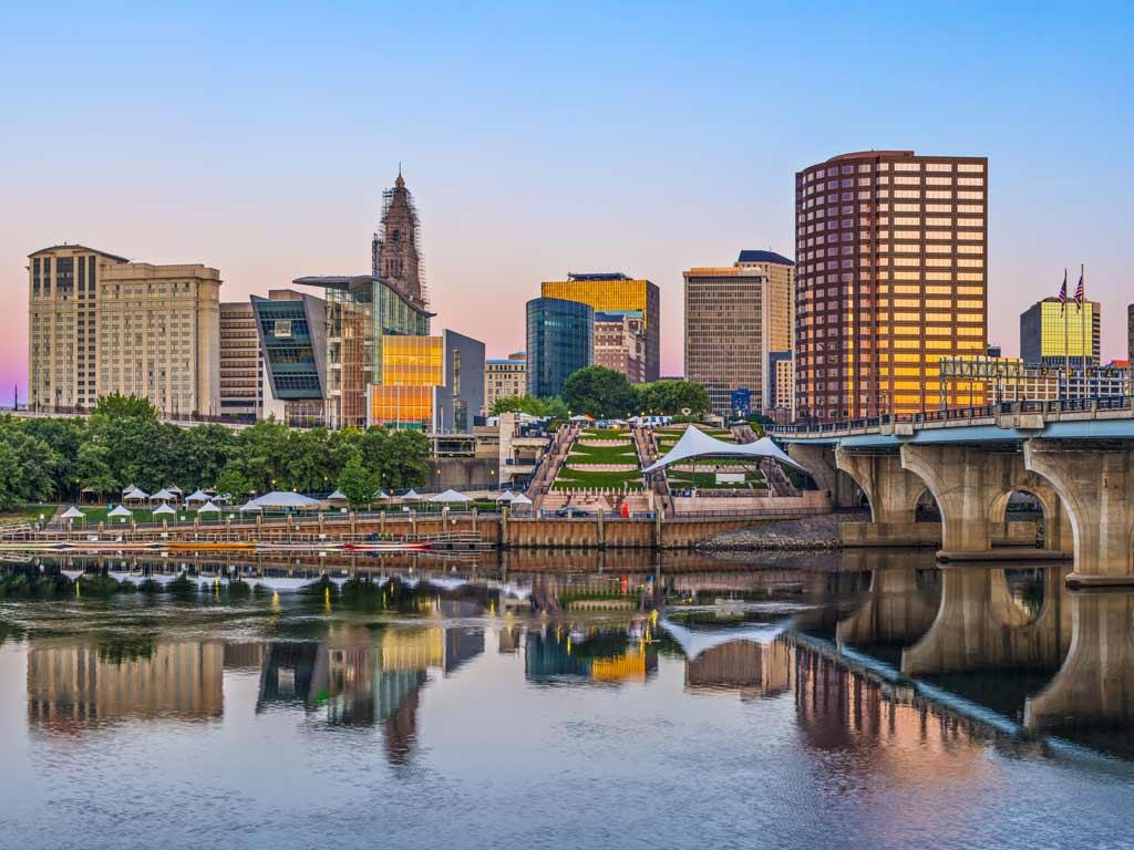 A view of the skyline of Hartford, the state capital of Connecticut, viewed from the Connecticut River at sunset, with buildings reflecting on the water