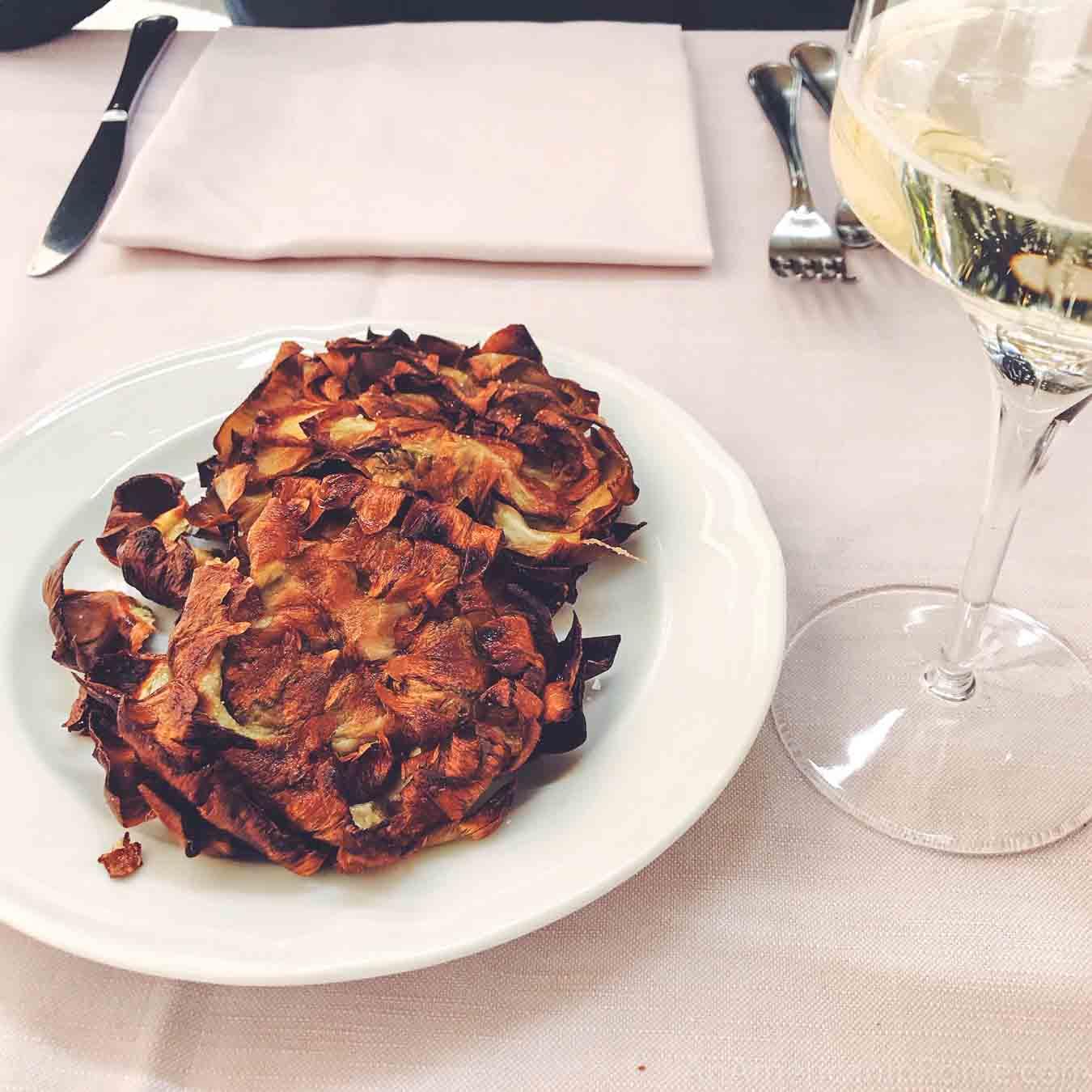 Two fried artichokes on a table with white wine