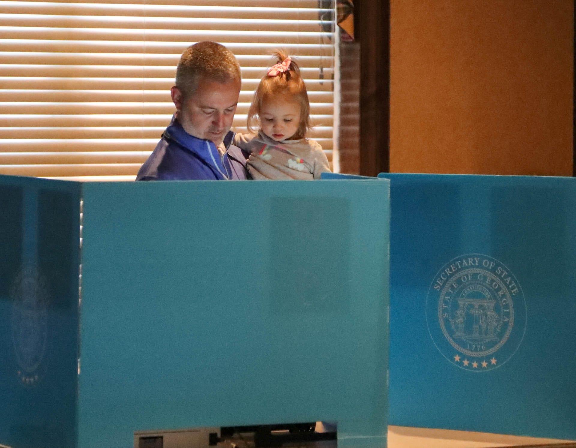 FILE - Alex Lowry holds his daughter as he casts his ballot on Tuesday, November 7, 2023 at First Presbyterian Church on Washington Avenue near Savannah, Georgia.