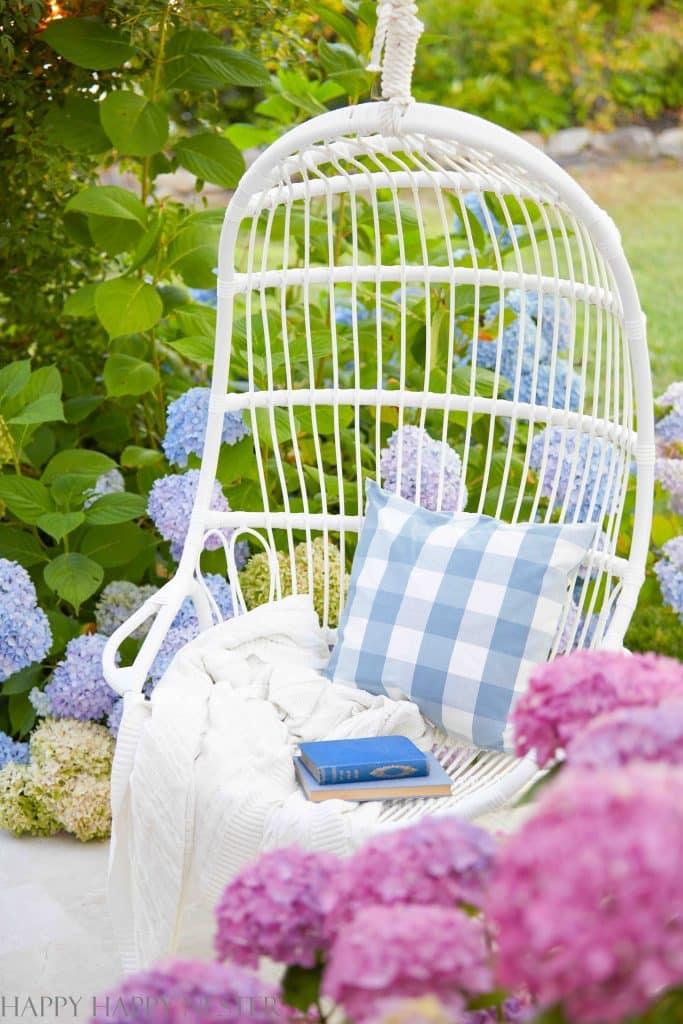 a white outdoor hanging chair position among some pink and blue flowering hydrangeas