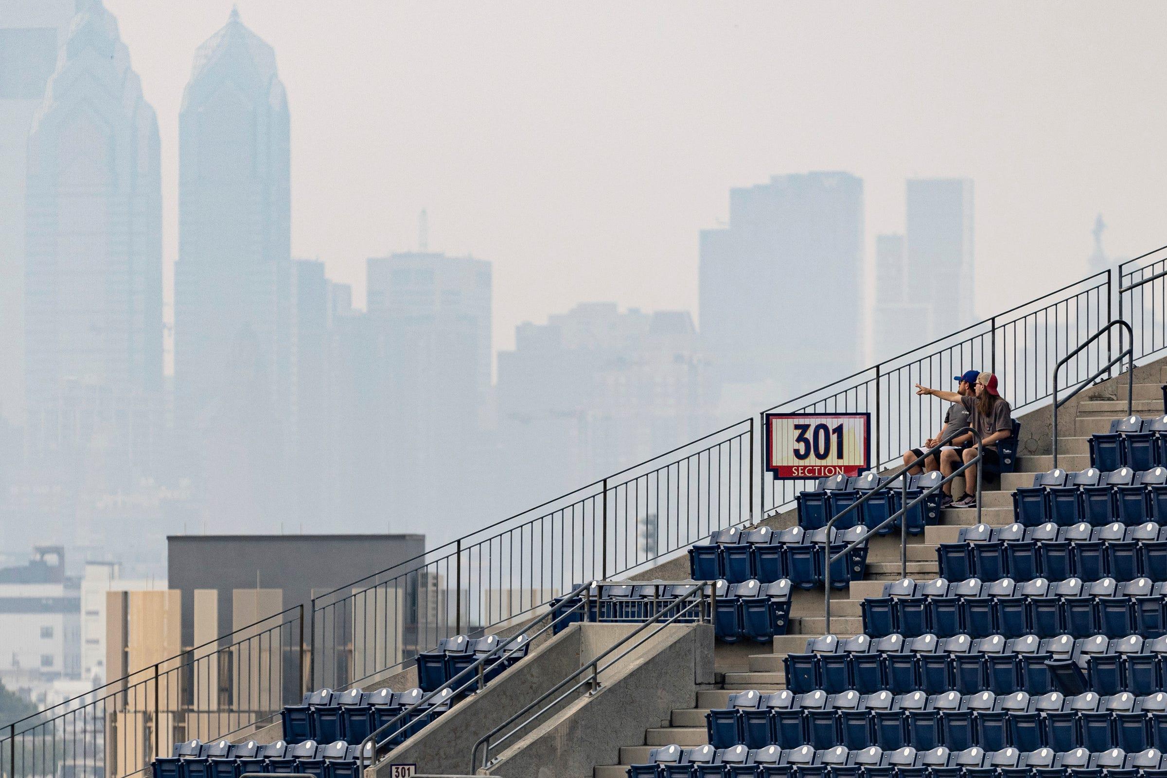 Two fans look out in the direction of center city Philadelphia as it is obscured by the smoke from Canadian wildfires before a game between the Phillies and the Tigers on Thursday, June 8, 2023, in Philadelphia.