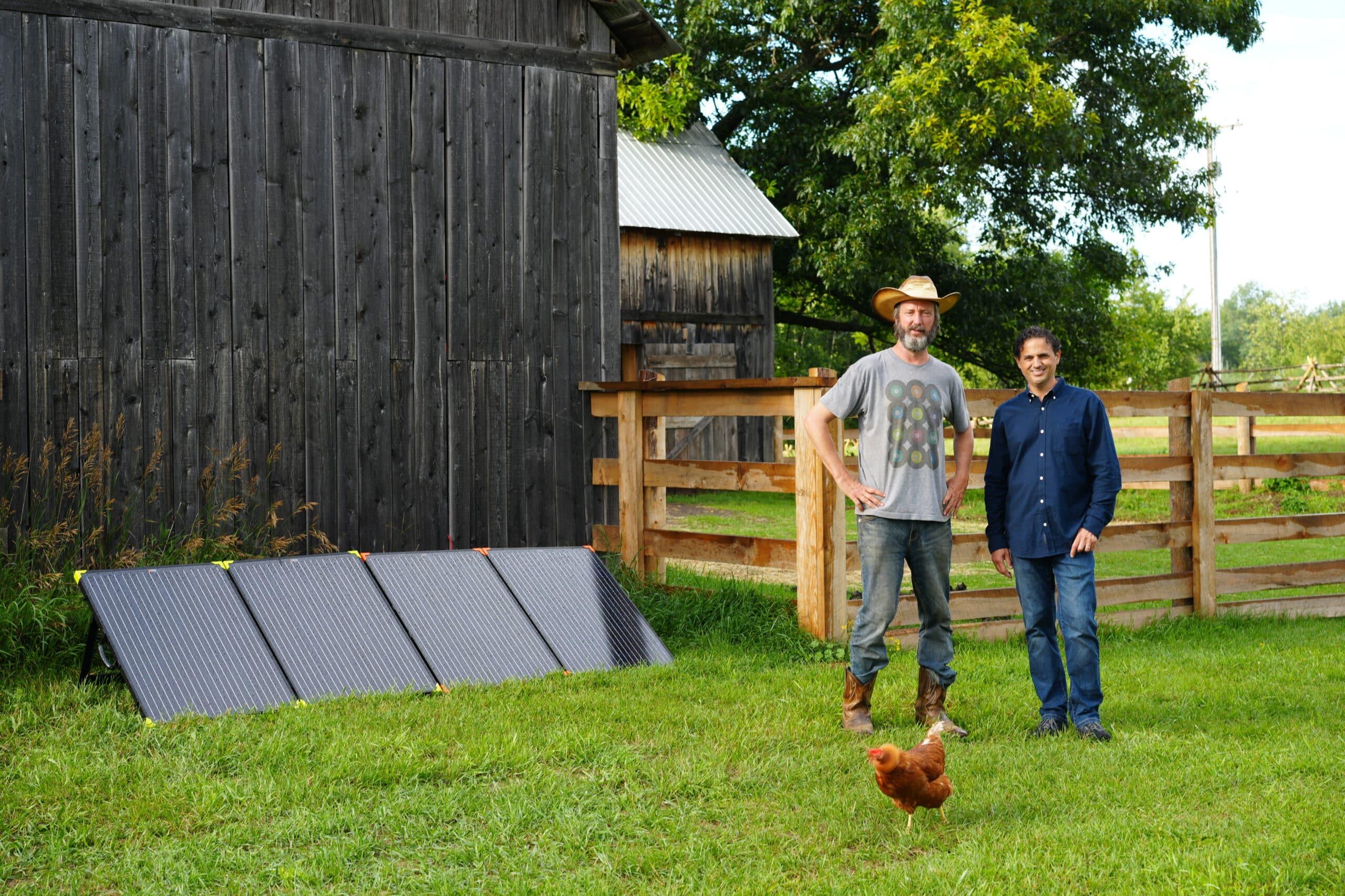 Tom Green and Denis Phares standing next to solar panels and a chicken