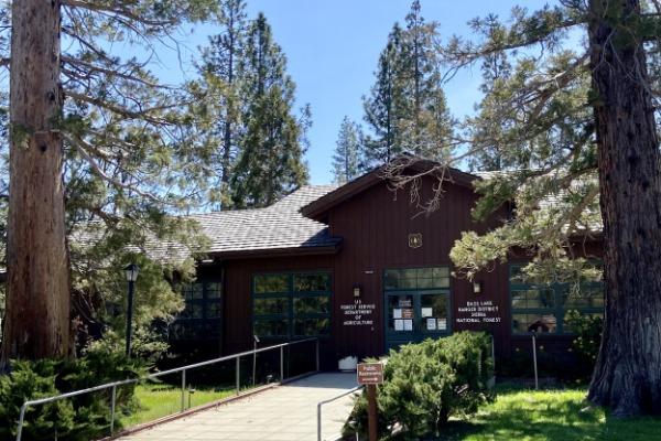 The Sierra National Forest headquarters is a brown wooden building flanked on two sides by large evergreen trees.