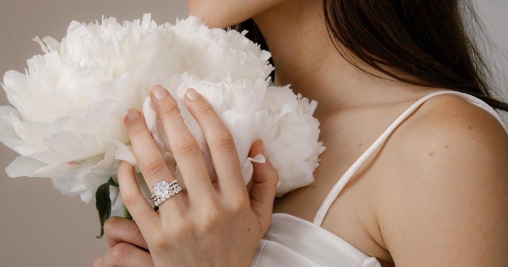 model holding white flowers and wearing stacked diamond rings