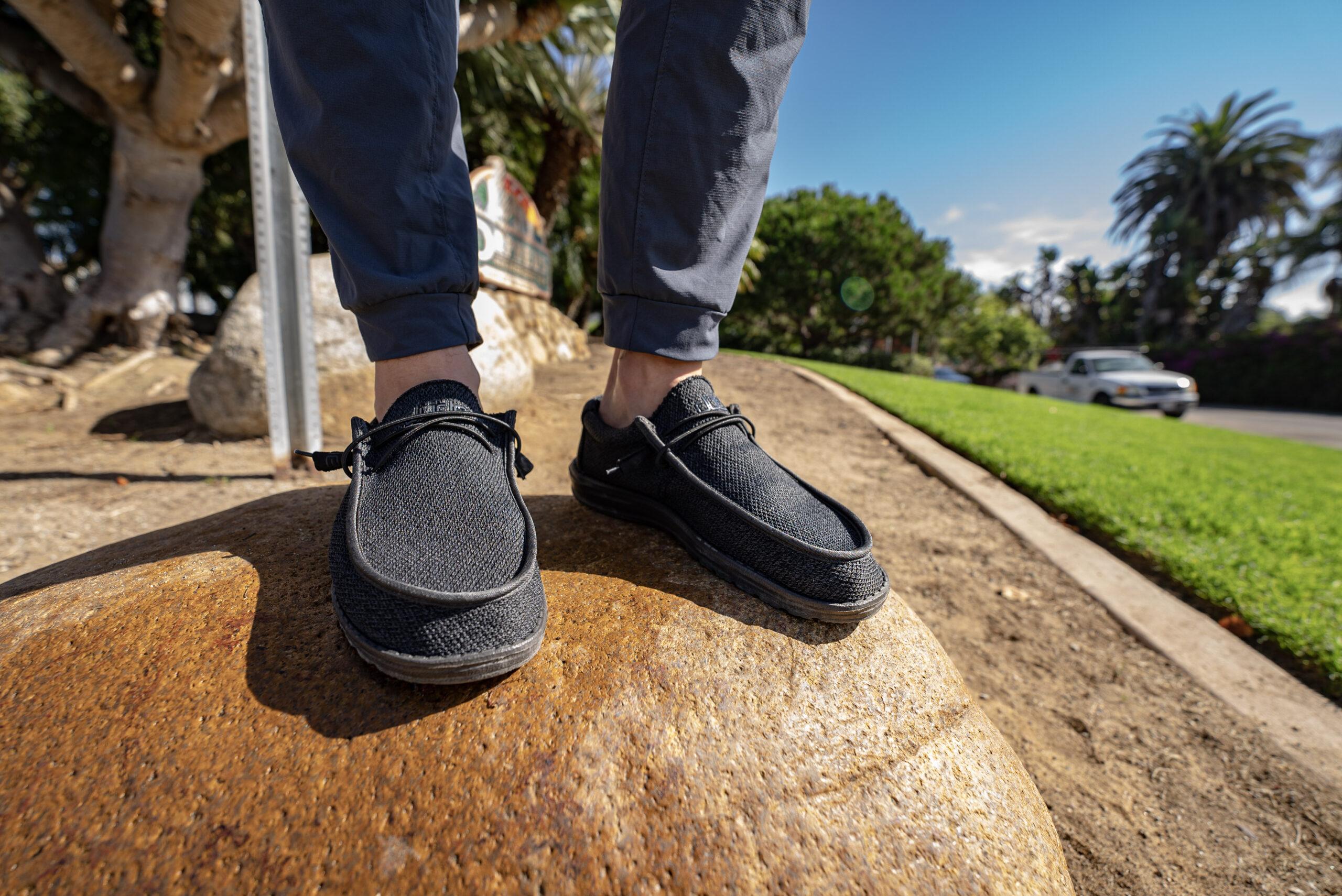 man standing on sidewalk wearing hey dude shoes and grey joggers