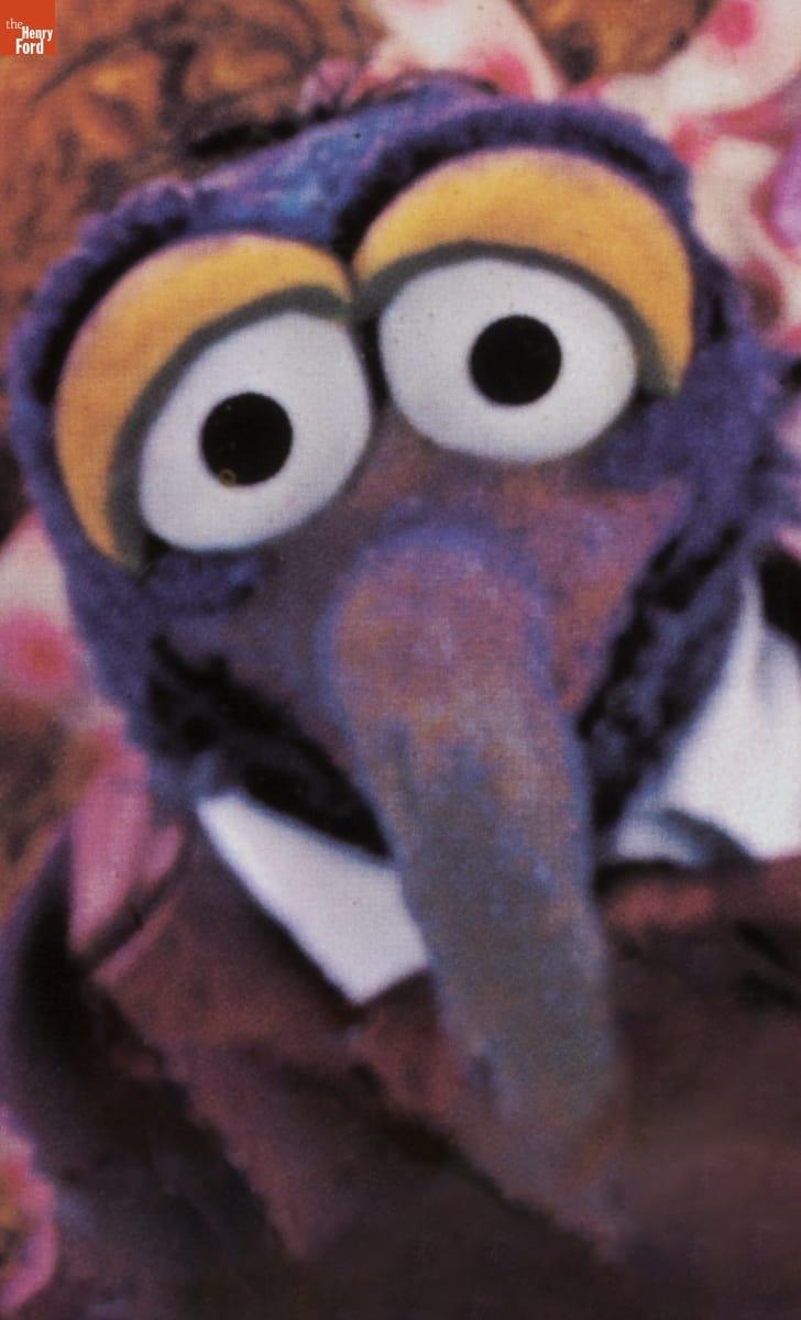 Head and shoulders of purple puppet with long hooked nose and large eyes