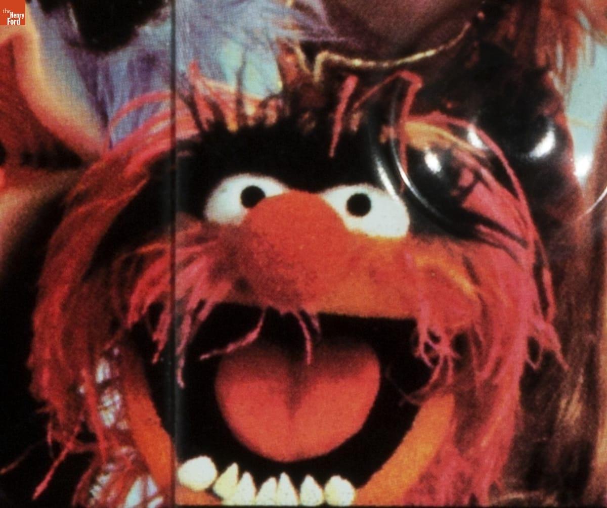 Puppet face with wispy red hair and mustache, bushy black eyebrows, round red nose, and pointy lower teeth