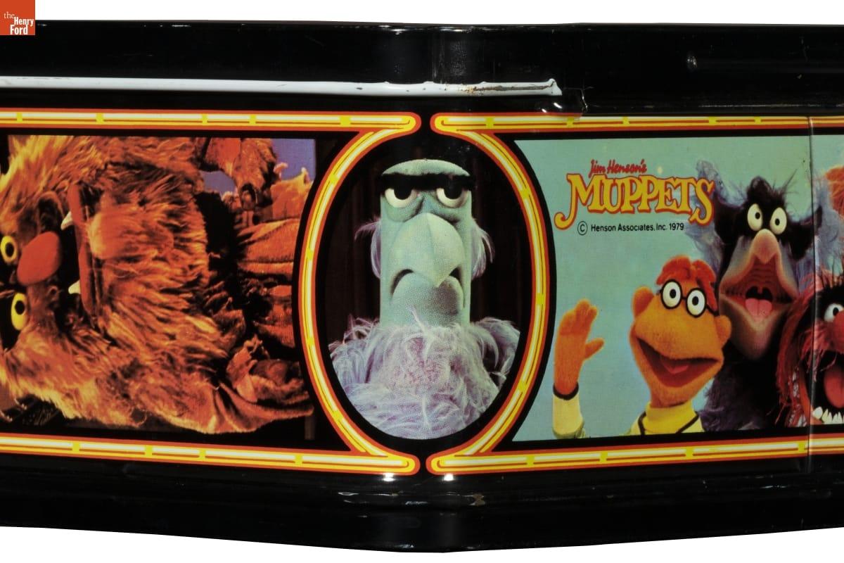 Corner of lunchbox with image of eagle puppet in center and other puppets on either side; also contains text