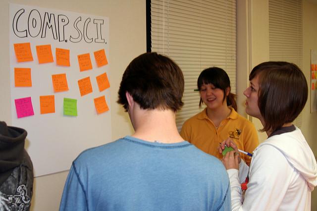 Photo of a group of students standing around a poster on the wall, where they
