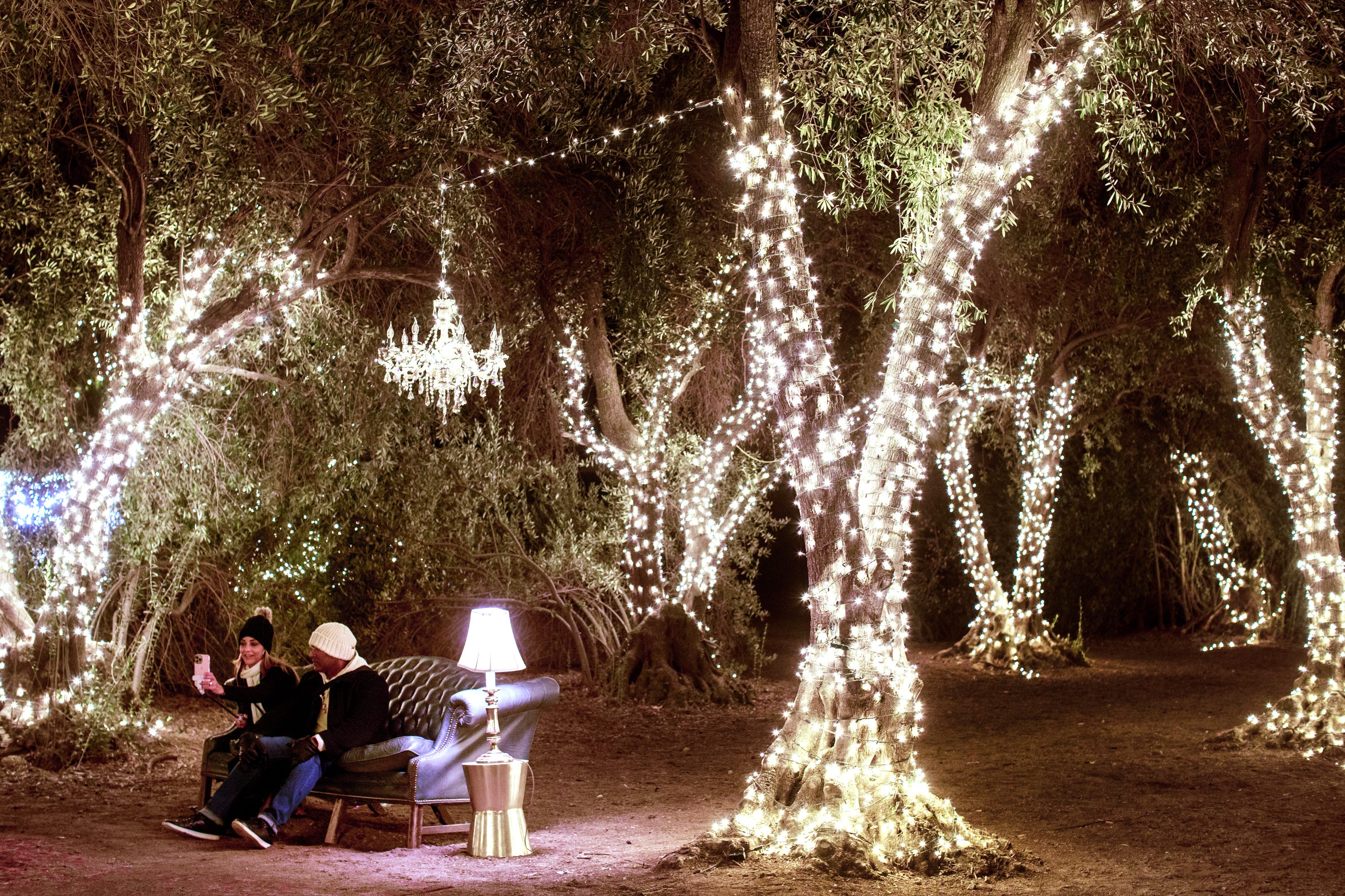 A couple sits amongst the olive trees during the Christmas Nights festival at 123 Farm in Beaumont, Calif., on Monday, Dec. 5, 2022.
