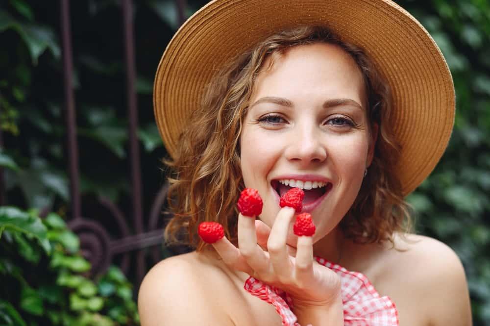 Close up young beautiful happy woman 20s wear pink dress hat put girl put raspberries on fingers eat