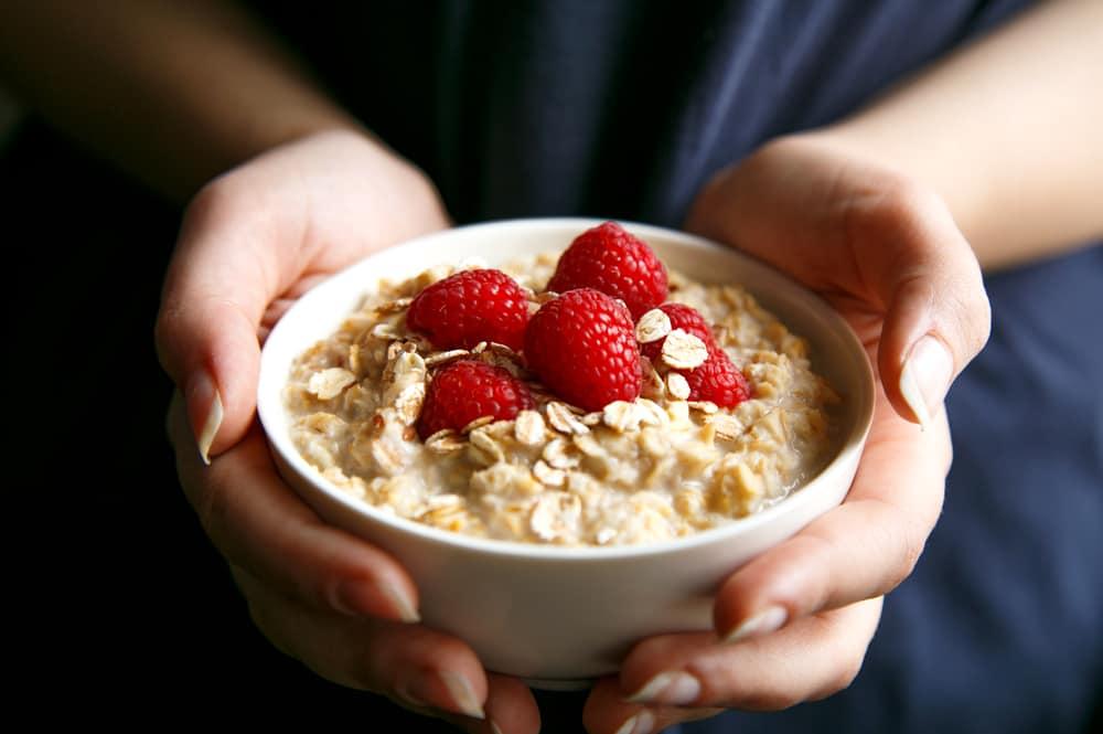 Woman hands holding healthy and natural breakfast, oatmeal and raspberries in a bowl